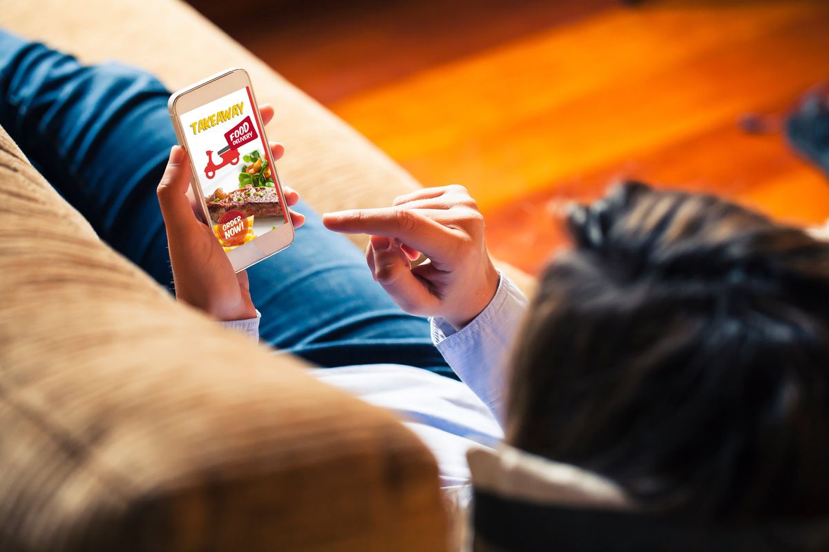 Woman laying on a couch with smartphone showing a food delivery app