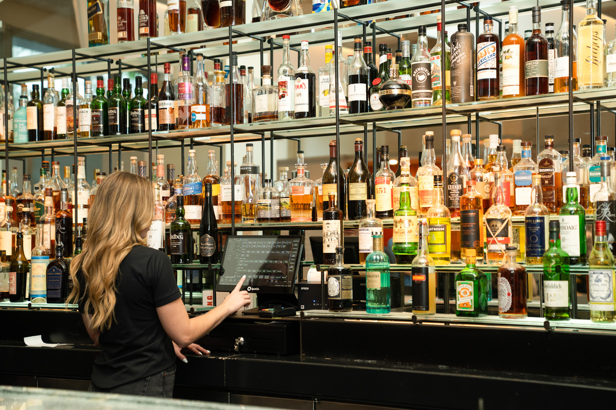 Woman using SpotOn bar POS system to order liquor at a bar to serve customers