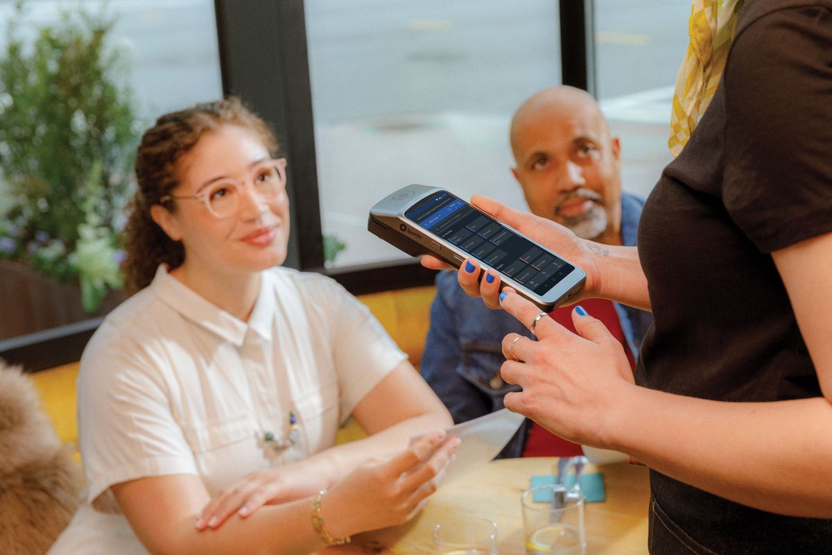 A restaurant server uses a handheld POS to take an order from guests