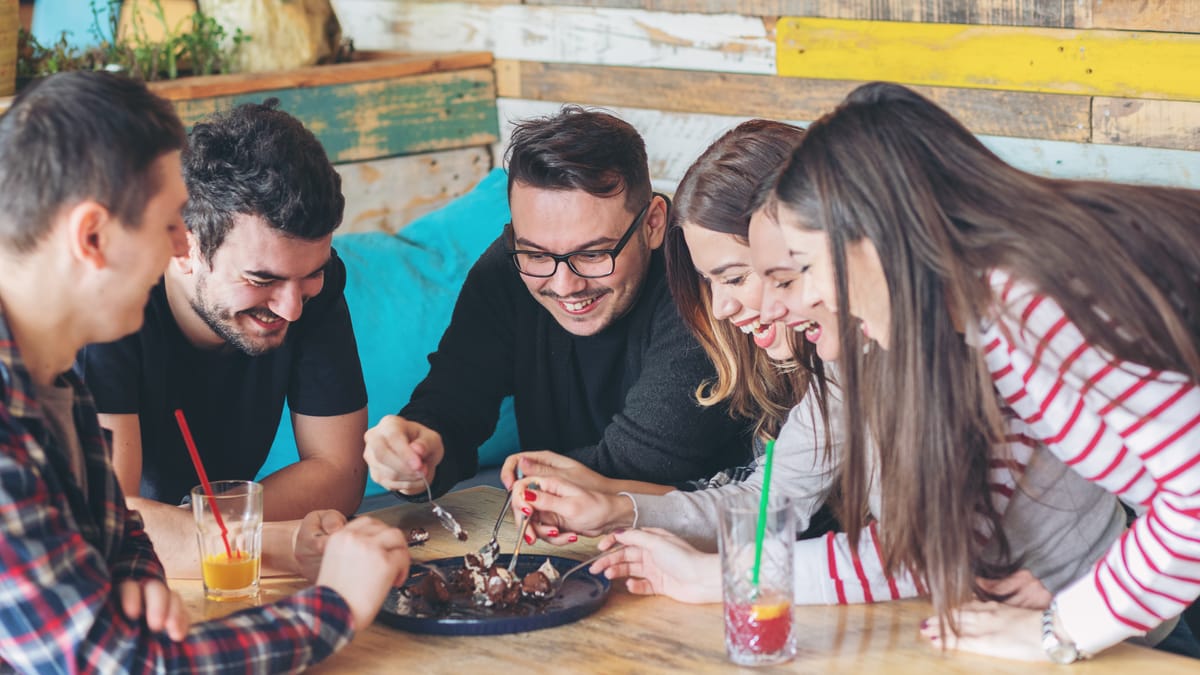 5 friends eating dessert at a restaurant and smiling from great customer service.