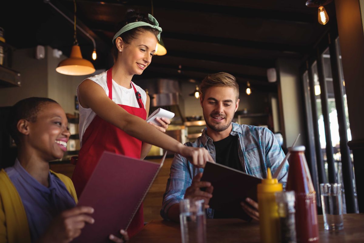 A restaurant server takes orders from two guests by hand