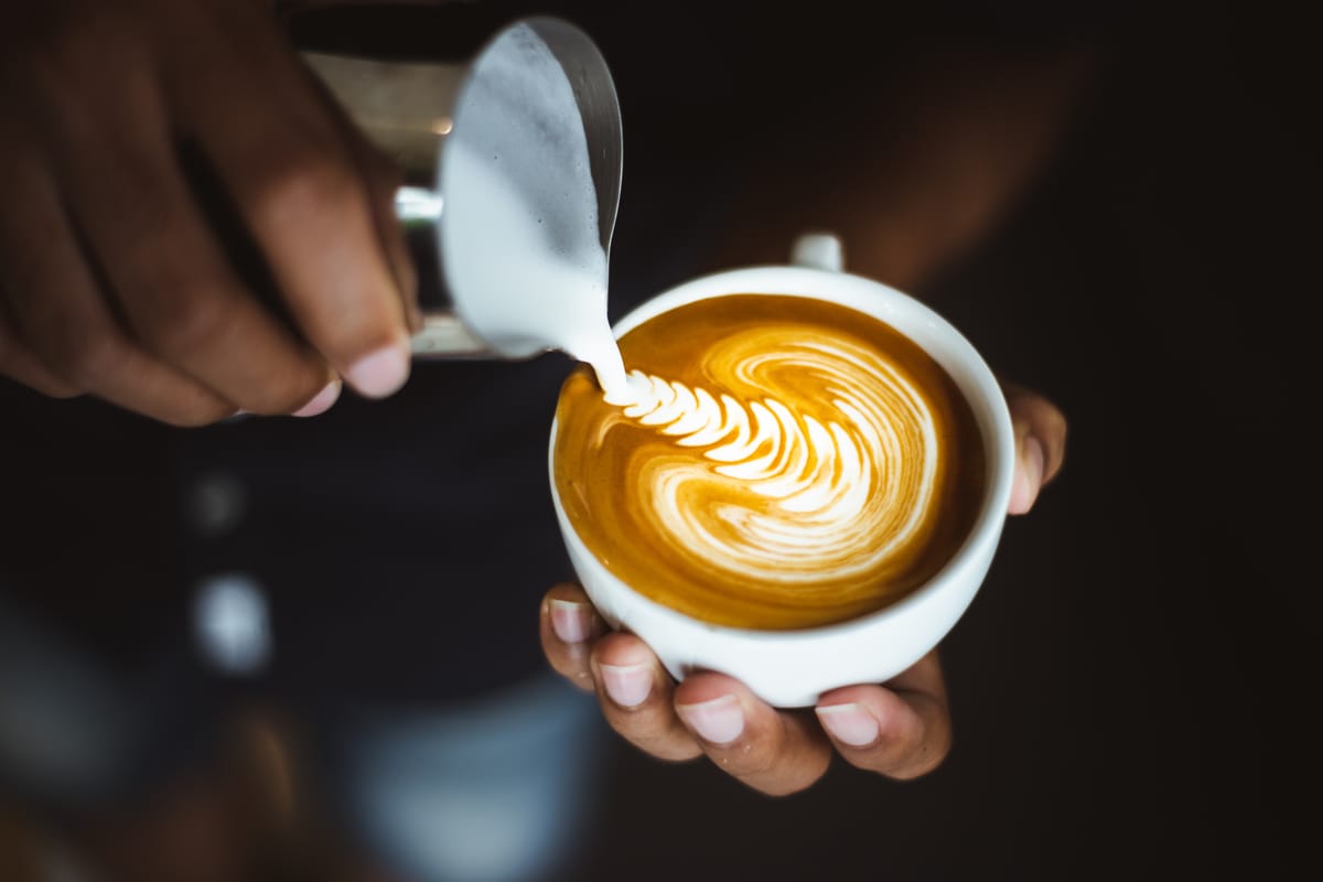 Barista at a coffee shop pouring hot milk froth into a cup of mocha.