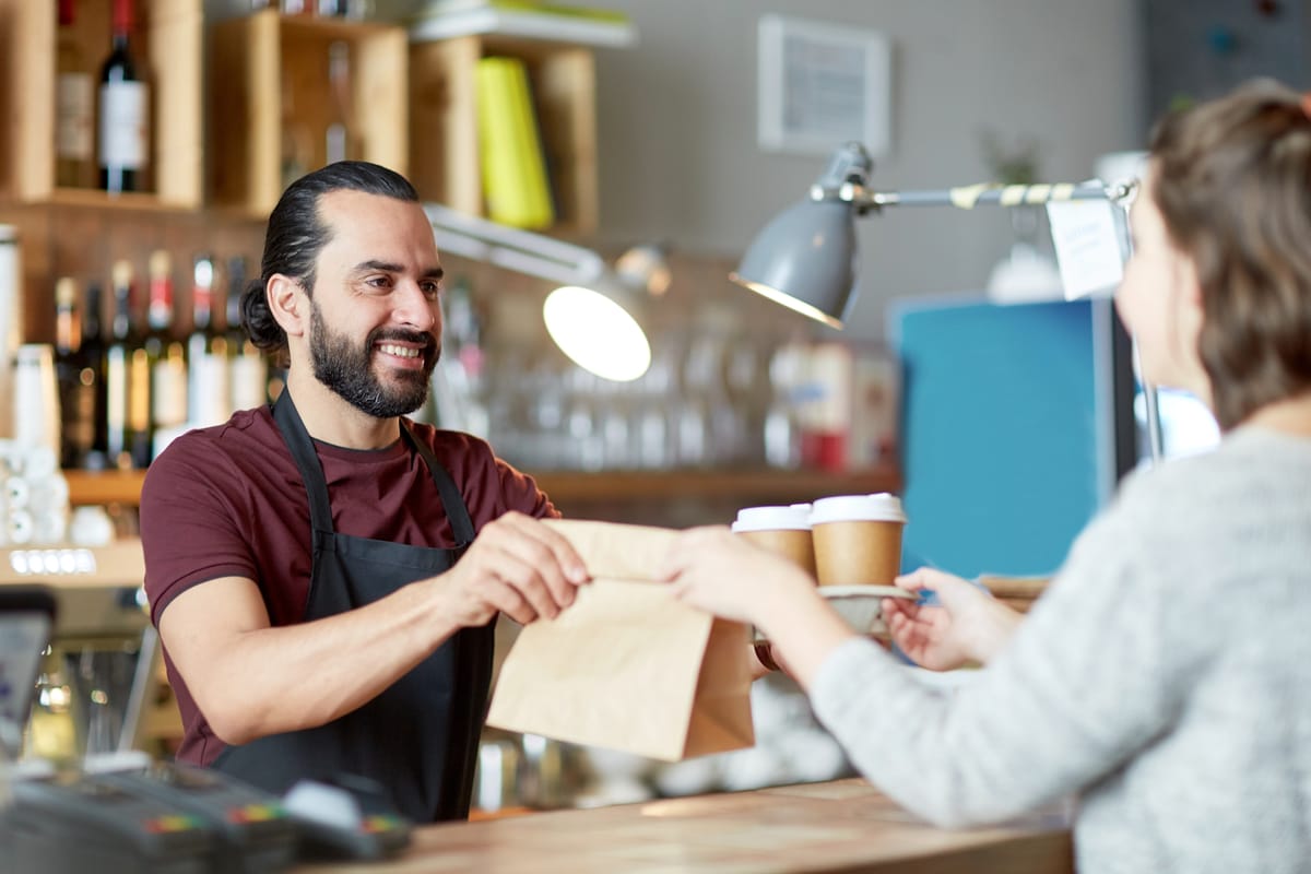 Man hands a woman her pickup order. The Skip the Stuff law aims to reduce plastics in restaurants.