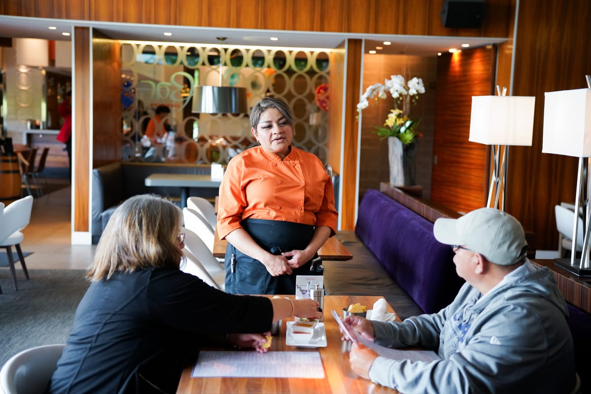 A restaurant server takes an order from two guests