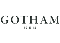 Black signiture  with capital letters on transparent background "GOTHAM" and below it there are two black lines between which is written with smaller black letters and numbers "12 E 12"