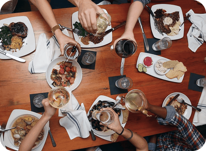 Restaurant guests raise glasses over a table filled with shared dishes.