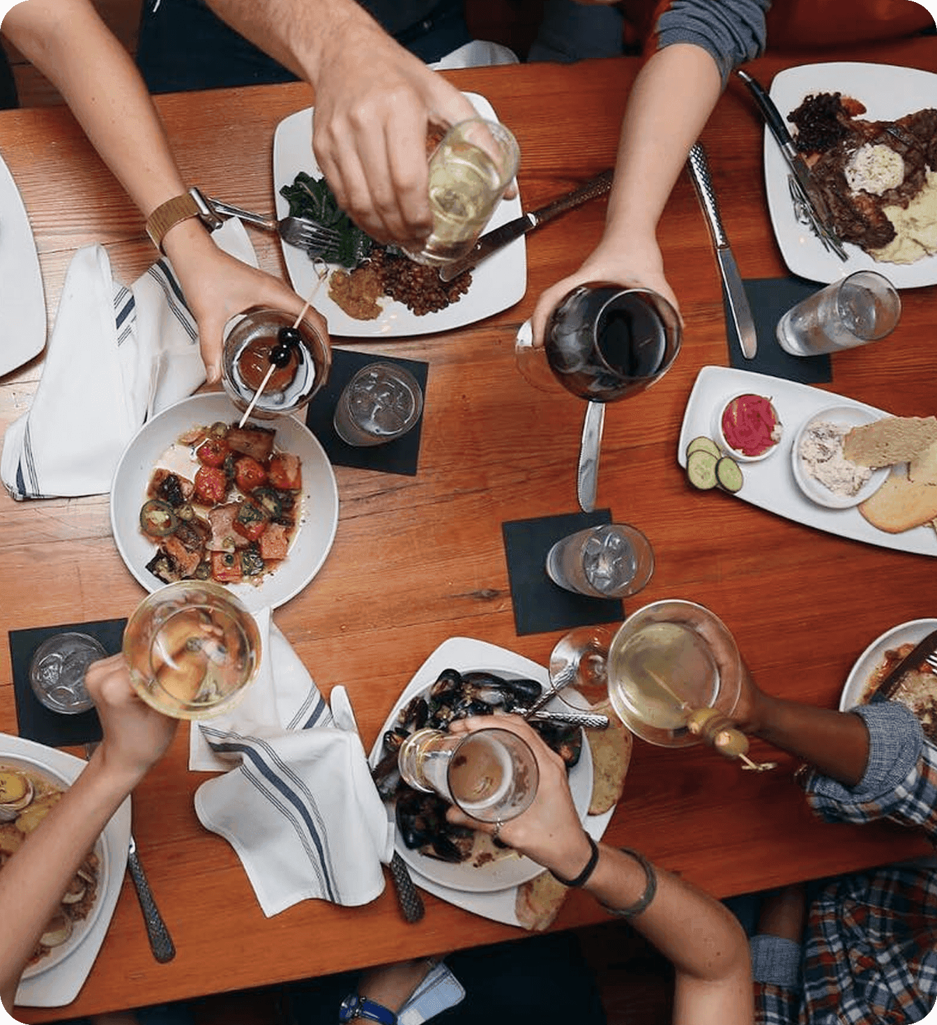Restaurant guests raise glasses over a table filled with shared dishes.