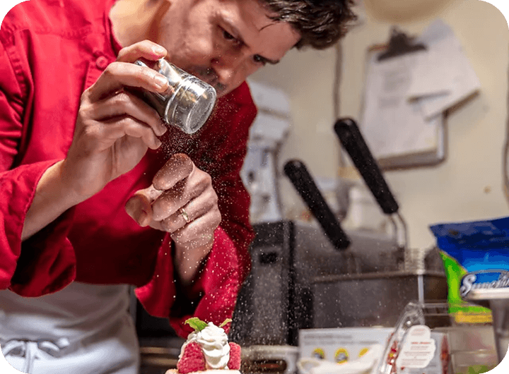 A chef dusts a raspberry-and-cream dessert with powdered sugar.