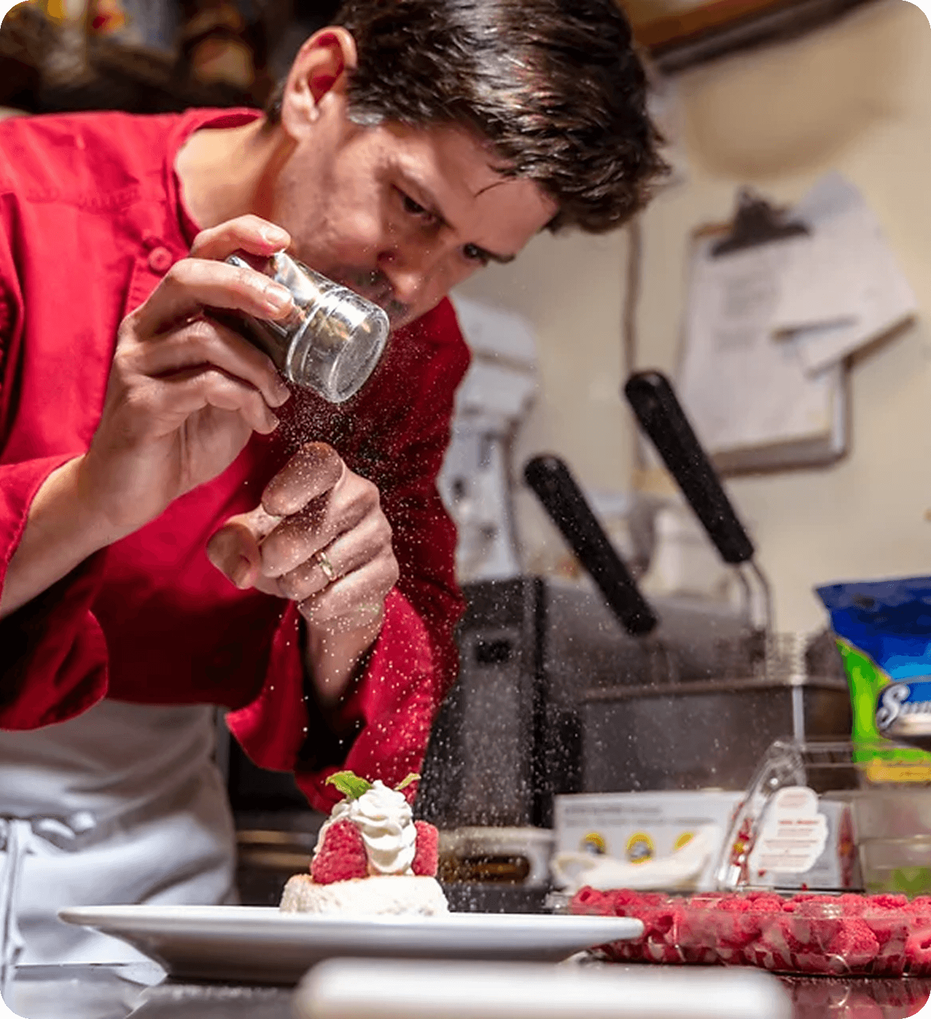 A chef dusts a raspberry-and-cream dessert with powdered sugar.