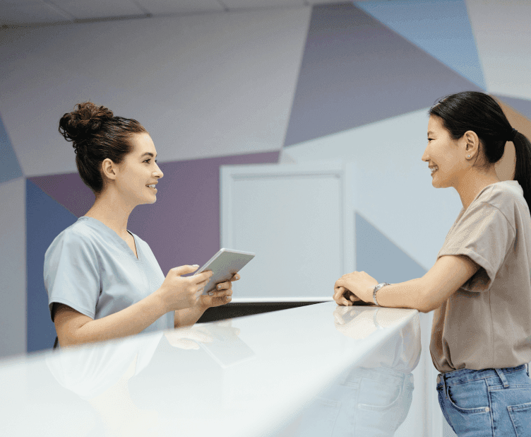 Healthcare professional in scrubs using tablet device while assisting patient at modern reception desk with geometric patterned wall