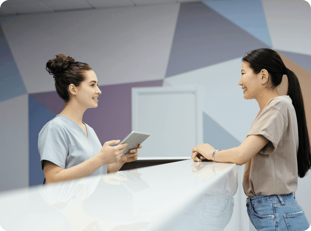 Healthcare professional in scrubs using tablet device while assisting patient at modern reception desk with geometric patterned wall