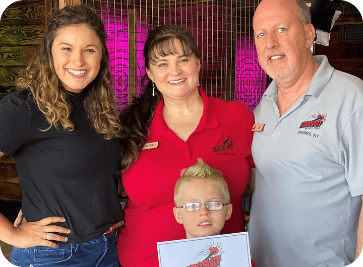Group of four smiling people at a restaurant, including a child holding a flyer.