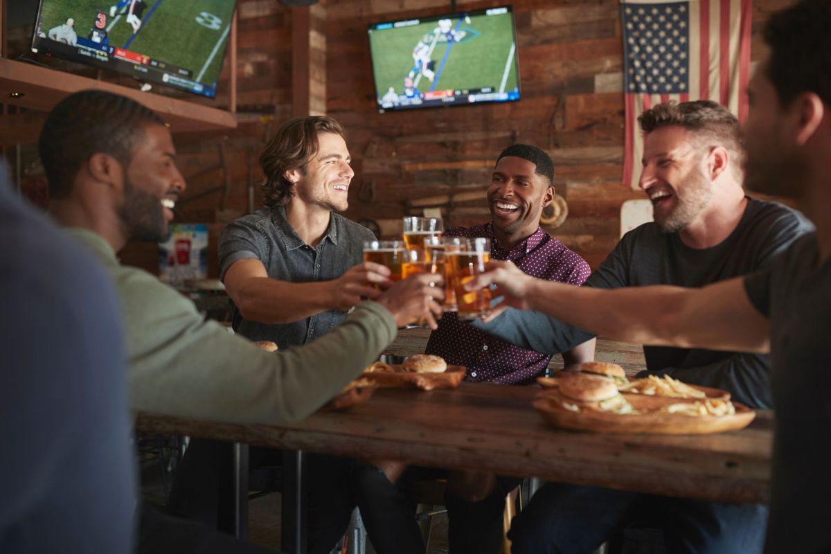 Four men toast with beer at a restaurant while the Super Bowl is on TV.